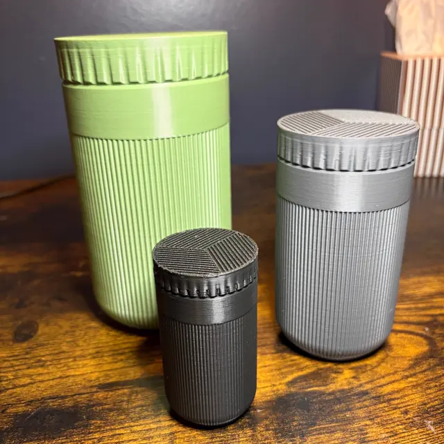 Three ribbed storage jars in olive green, grey and black with patterned lids